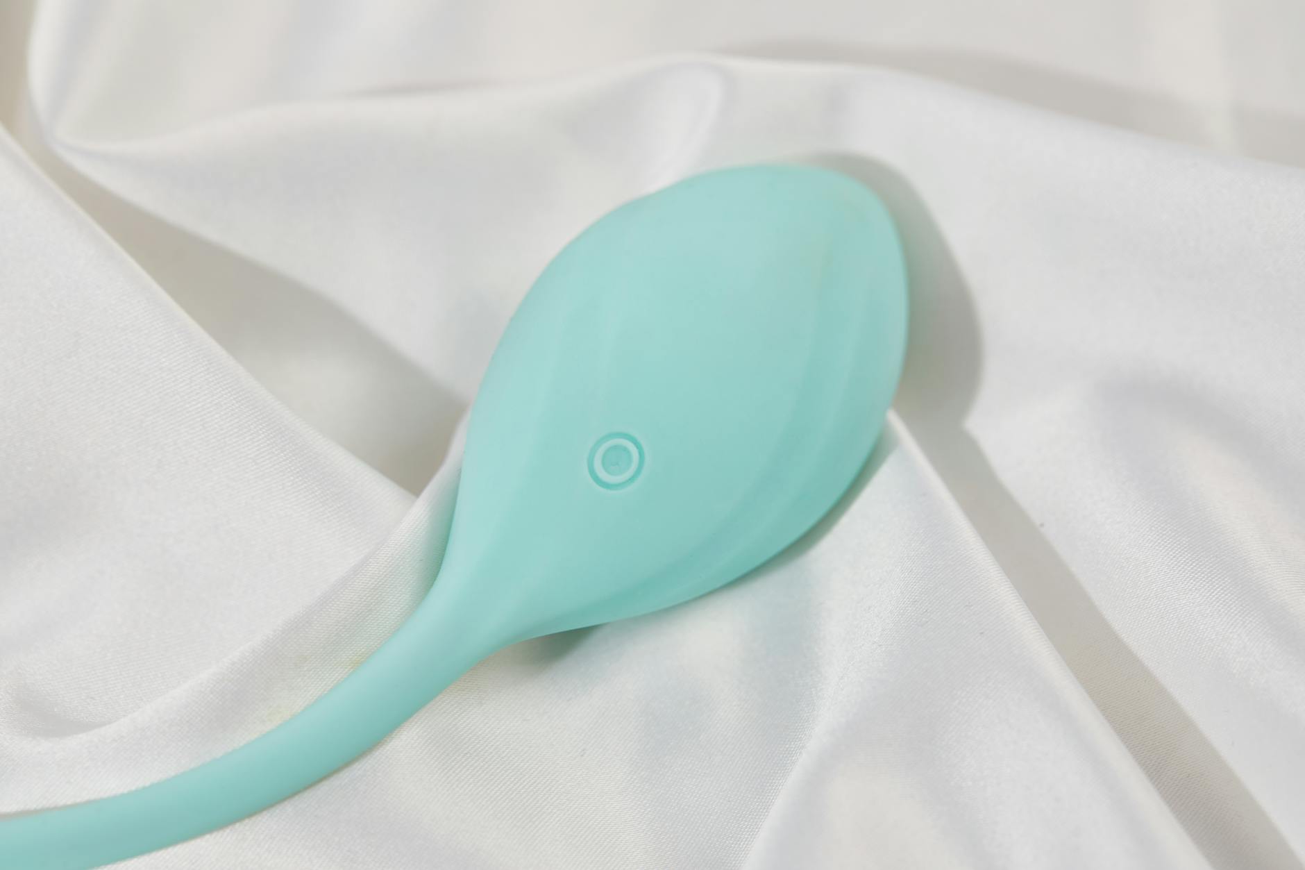 A smooth teal lemon vibrator resting on white silk fabric