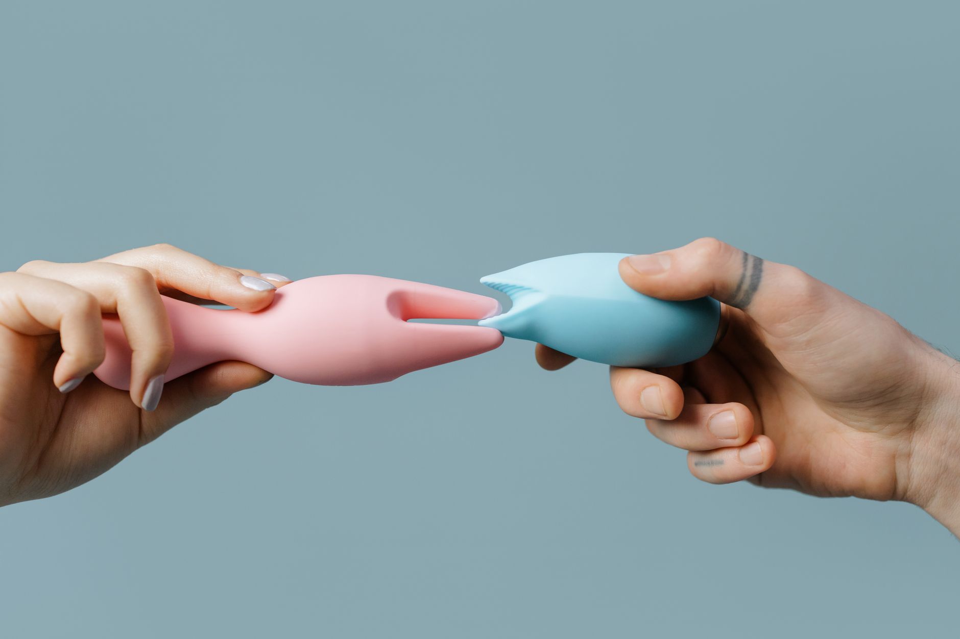 Hands holding pastel-colored silicone toys for adult pleasure and exploration