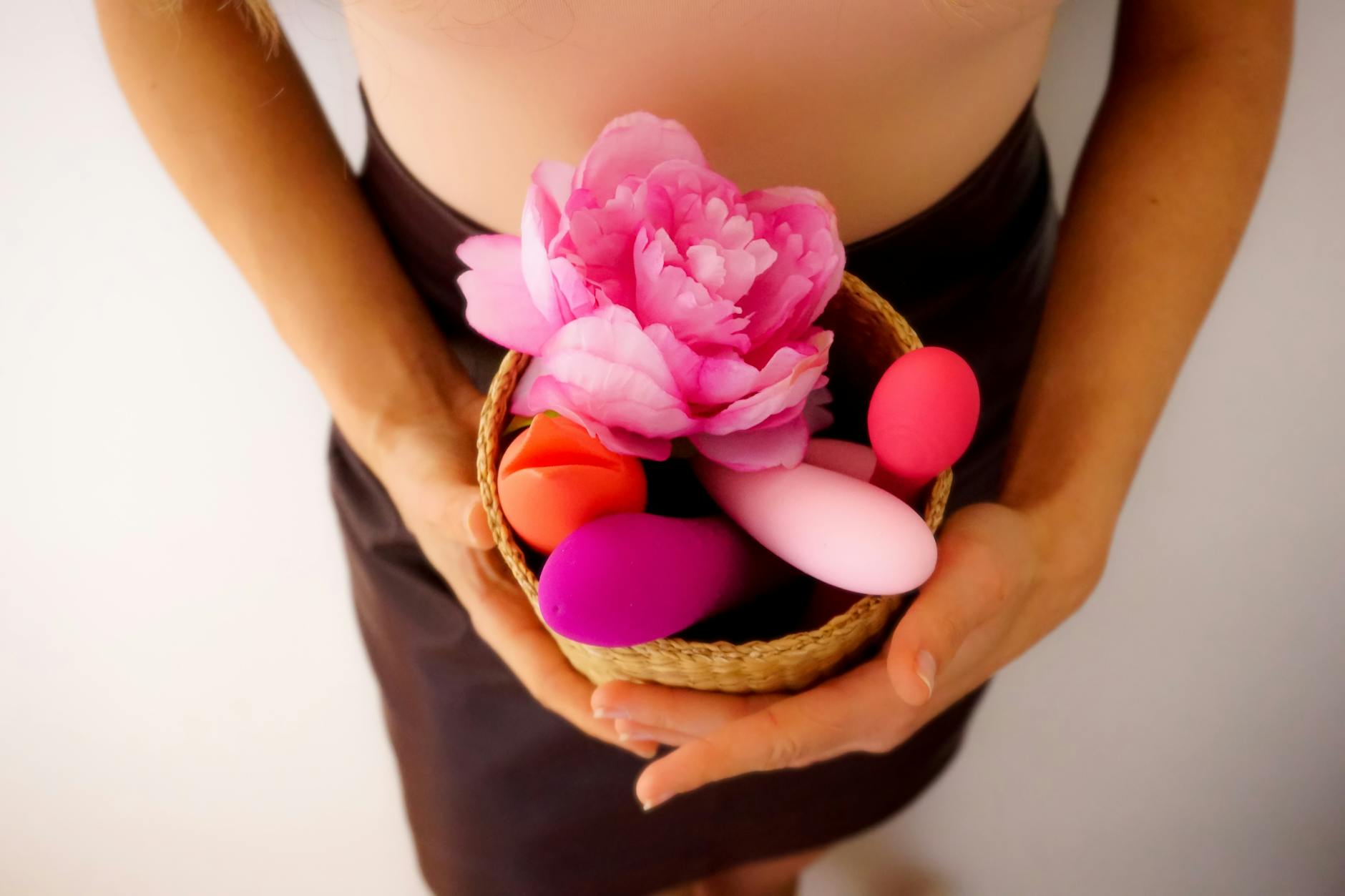 A collection of colorful vibrators in a basket with a pink flower, representing diverse pleasure tools